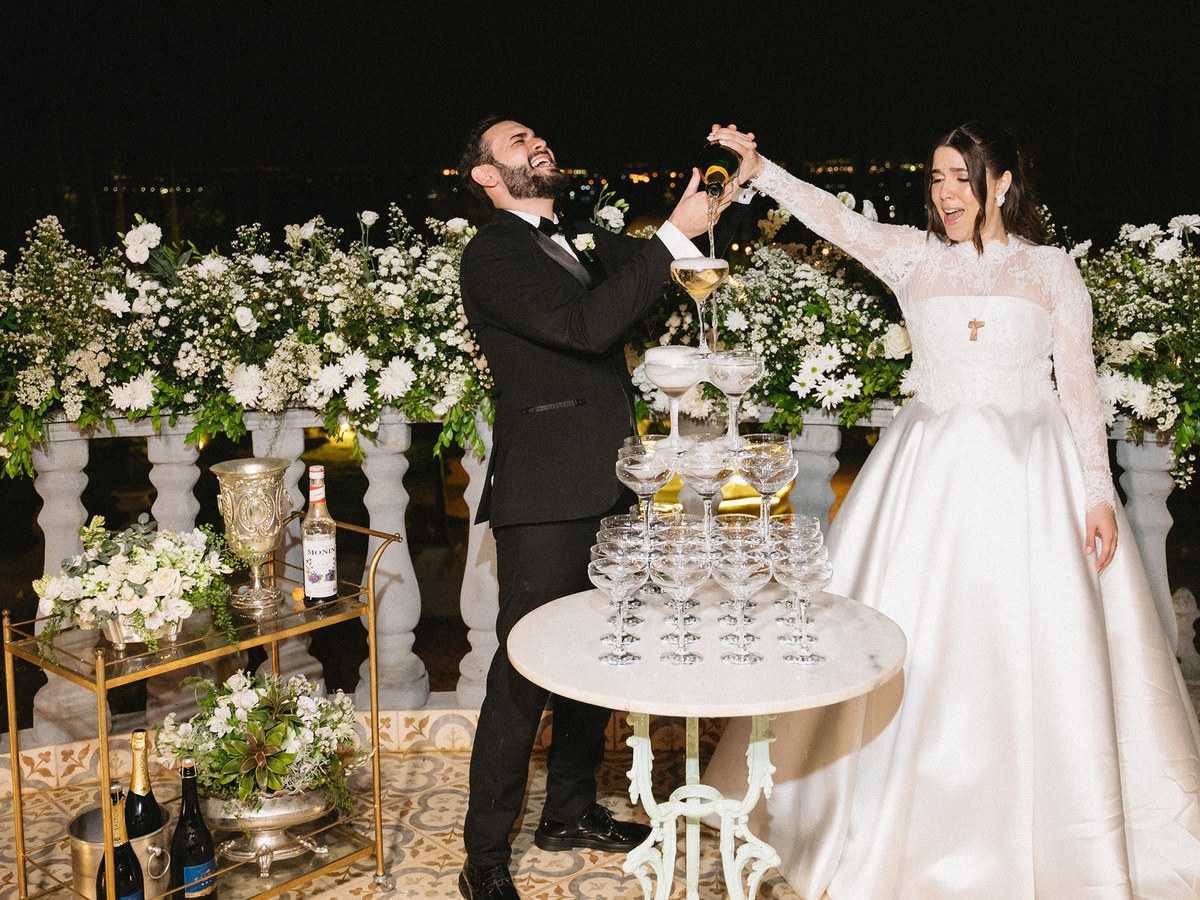 Noivos servindo uma torre de tacas de champanhe em casamento atendido pela Herms